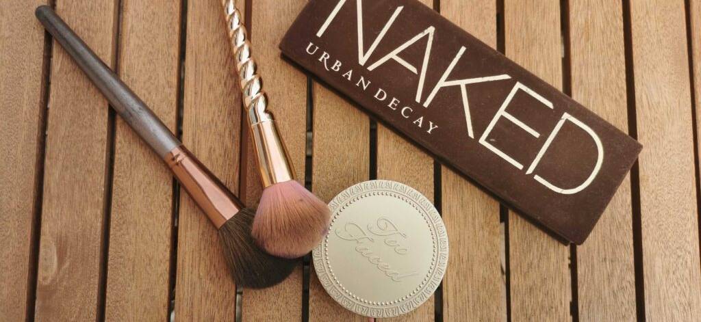 Bronze-Make-up im Test: Zwei Schminkpinsel liegen neben Schminke und einer Puderdose auf einer Holzoberfläche.