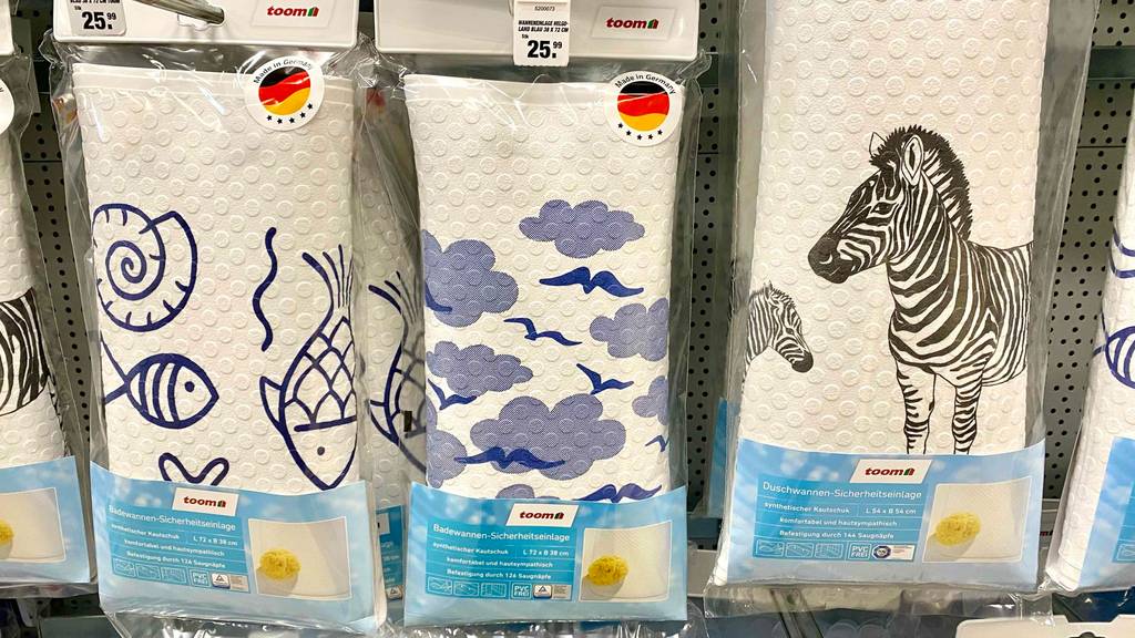 Badewannenmatten im Test: drei Toom Modelle mit unterschiedlichen Motiven hängen original verpackt nebeneinander an einem Verkaufsregal.