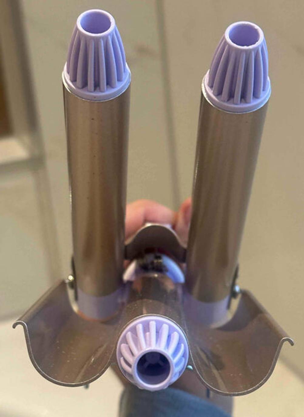 Welleneisen im Test: Hand hält ein geöffnetes Modell vor dem Hintergrund eines gefliesten weißen Badezimmers.