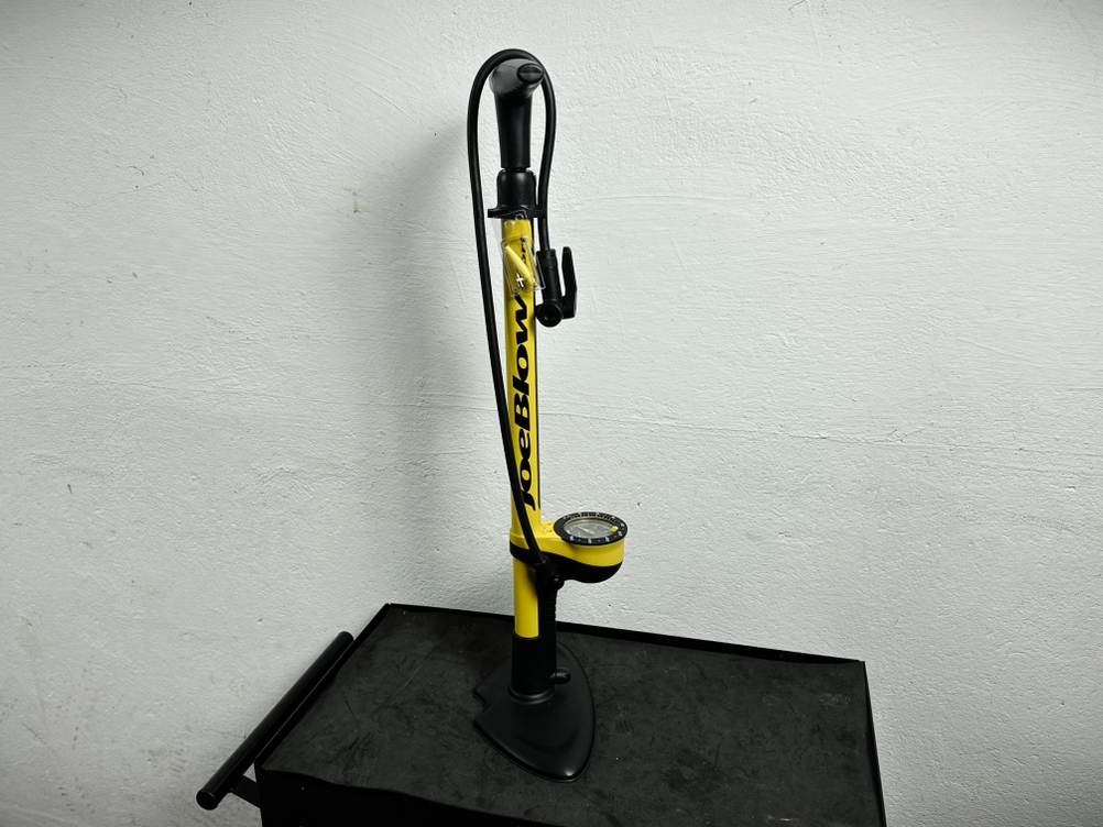 Die Topeak Joe Blow Sport III Fahrradpumpe steht aufrecht auf einem Werkstatttisch. Das Gehäuse ist gelb-schwarz.