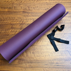 Die Toplus-Yogamatte liegt neben ihrem Tragegurt auf einem Holztisch