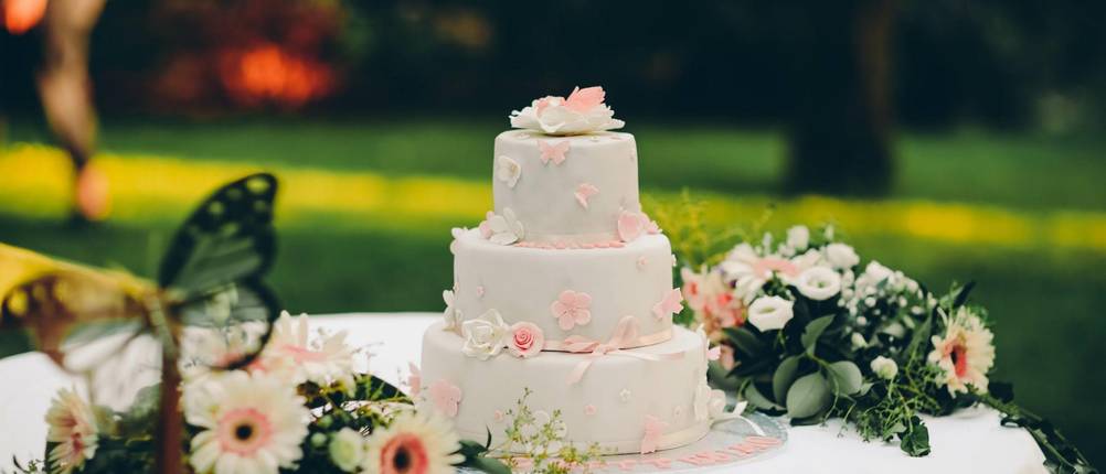 Torten-Deko-Test: dreistöckige Hochzeitstorte im Freien, auf einem Tisch mit Blumen-Arrangement daneben