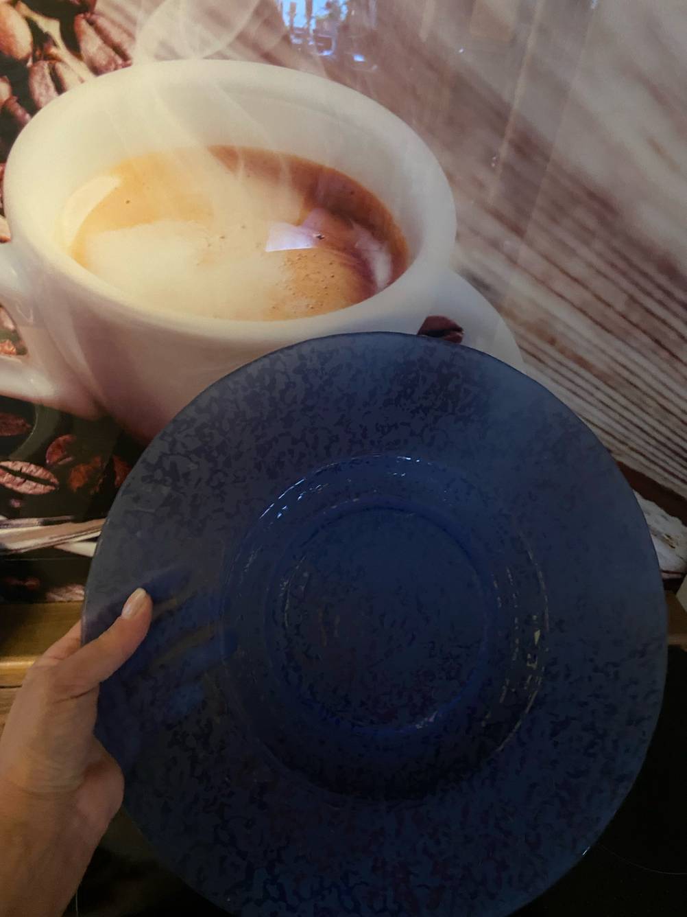 Getestet: Eine Hand hält die Tortenplatte vor ein Plakat mit einer Kaffeetasse.