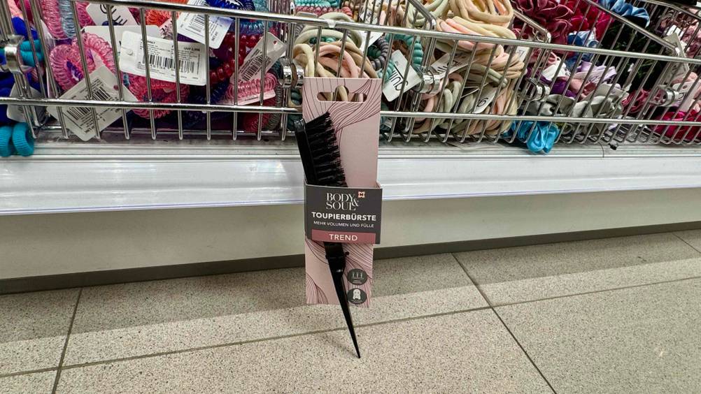 Vor einem Regal mit Haarbändern steht die getestete Toupierbürste am Boden.