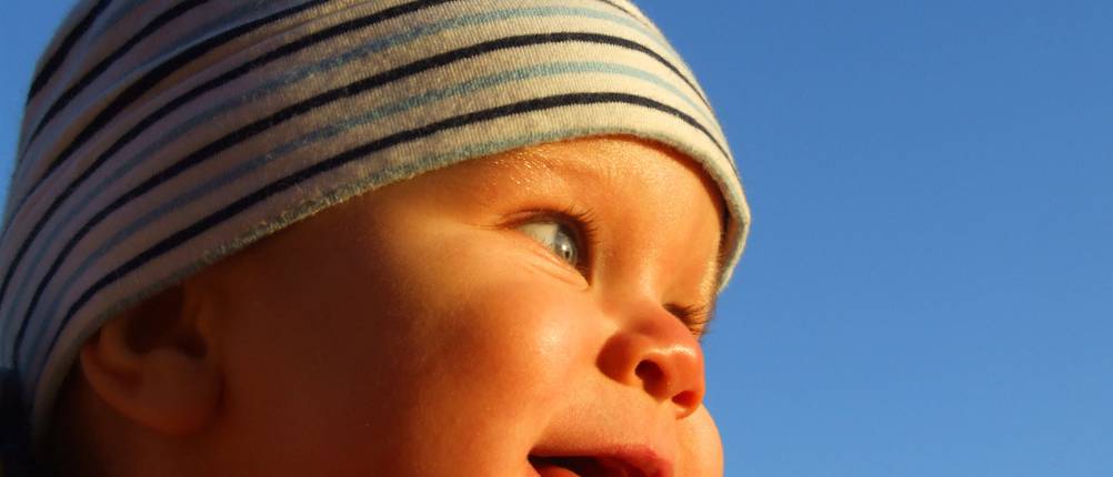 tragejacke-herren-test:: Baby mit gestreifter Mütze schaut in Sonnenuntergang.