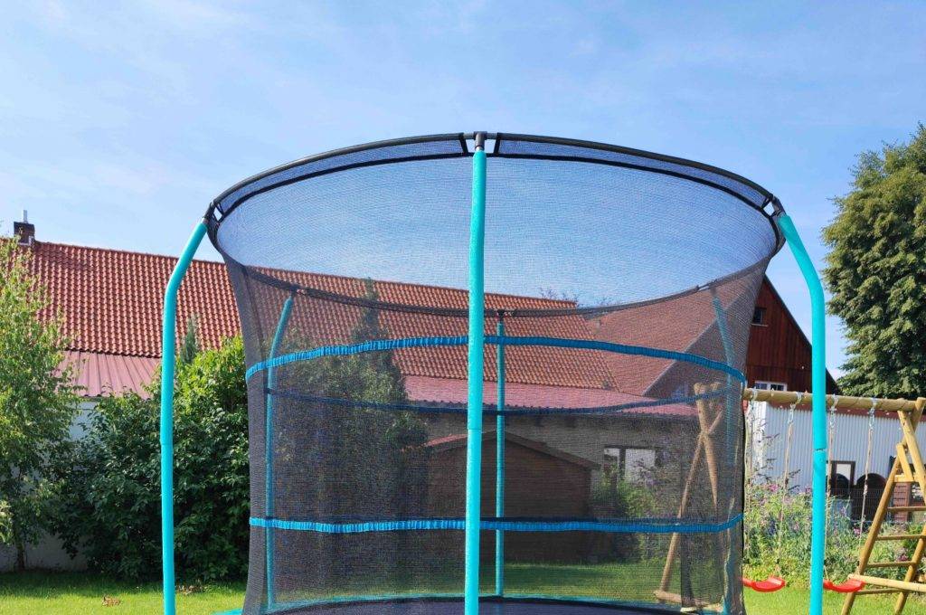 Ein getestetes Trampolin steht im Garten neben zwei Schaukeln.