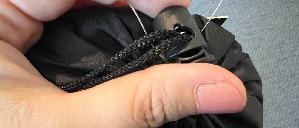 Zwei Finger öffnen Druckknopf des Transportbeutels beim Traveler's-Pal-Hüttenschlafsack