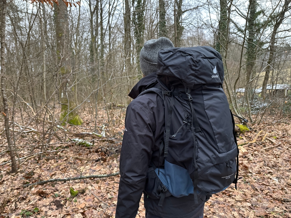 Ein Wanderer trägt den Deuter Aircontact Lite 50+10 auf dem Rücken. Die Umgebung ist ein bewaldeter, leicht verschneiter Pfad.
