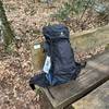 Der Deuter Aircontact Lite 50+10 Trekkingrucksack steht auf einer Holzbank im Wald. Das Modell ist vollständig bepackt.