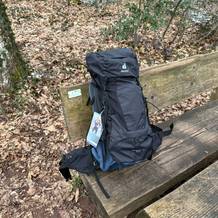 Der Deuter Aircontact Lite 50+10 Trekkingrucksack steht auf einer Holzbank im Wald. Das Modell ist vollständig bepackt.