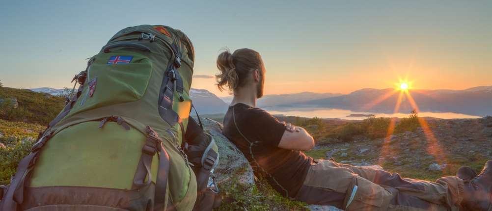 Trekkingrucksack - Mann macht Pause und lehnt gegen einem Stein und betrachtet den Sonnenuntergang