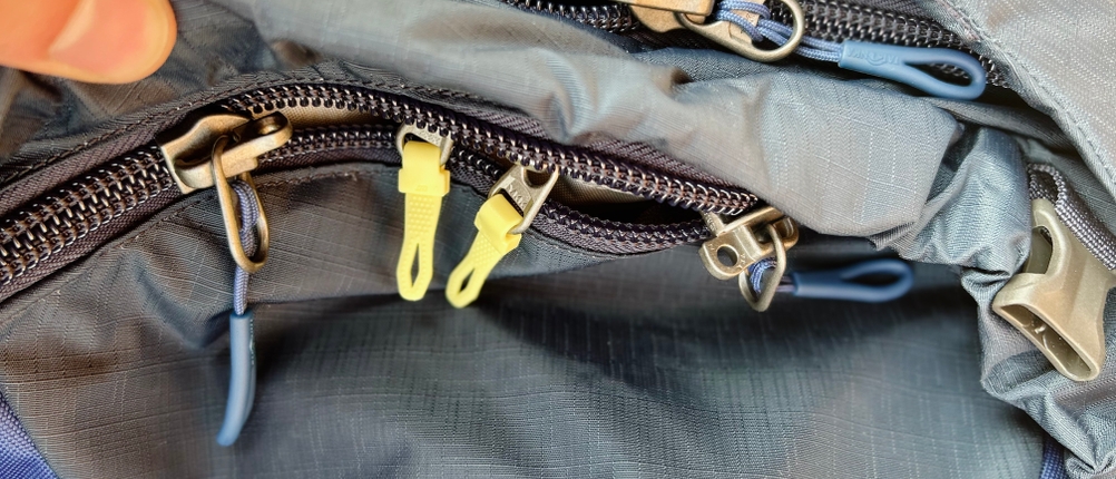 Mehrere Reißverschlüsse und Fächer des Tatonka Yukon 60+10 sind geöffnet zu sehen. Die Zipper sind farblich markiert.