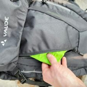 Ein hellgrüner Beutel wird in das Frontfach des Vaude Asymmetric 42+8 gesteckt. Der Reißverschluss ist offen.