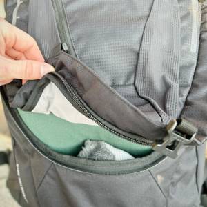 Ein Reißverschluss am Vaude Asymmetric 42+8 wird geöffnet. Kleidung und Ausrüstung im Hauptfach sind sichtbar.
