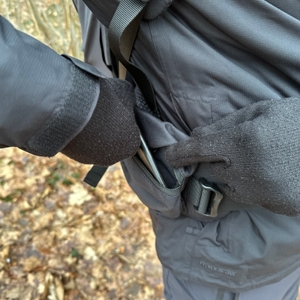 Ein Finger zeigt auf die Reißverschlusstasche im Hüftgurt des Vaude Asymmetric 42+8. Die Tasche ist leicht zugänglich.