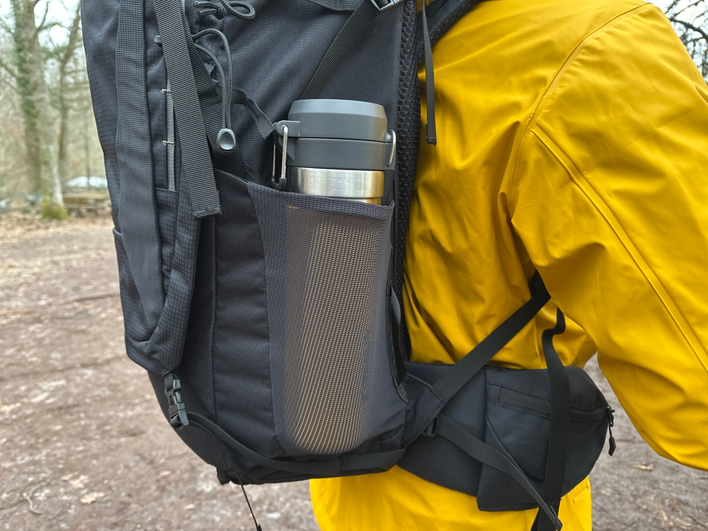 Seitenansicht des Vaude Asymmetric 42+8 mit Thermosflasche in der Netztasche. Die elastische Seitentasche liegt direkt oberhalb des Hüftgurts.