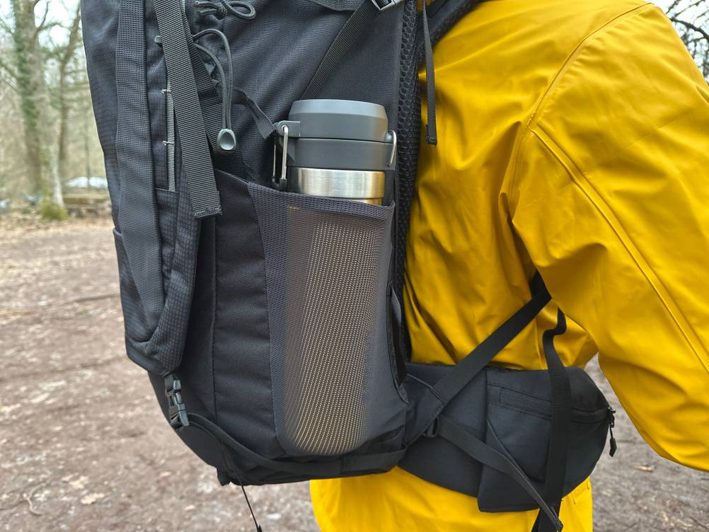 Seitenansicht des Vaude Asymmetric 42+8 mit Thermosflasche in der Netztasche. Die elastische Seitentasche liegt direkt oberhalb des Hüftgurts.