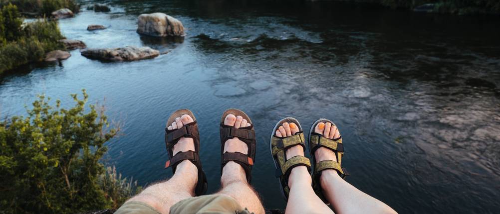 Trekkingsandalen-Unisex-Test: Zwei Personen mit Trekkingsandalen sitzen am Wasser. 