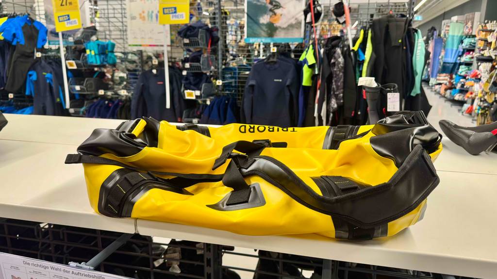 Im Test: Die wasserdichte Reisetasche in Gelb mit schwarzen Aplikationen liegt auf einem Verkaufsschrank im Sportwarengeschäft.