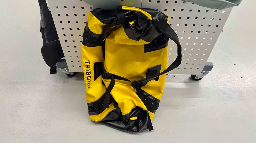 Die getestete, wasserdichte Reisetasche in Gelb mit schwarzen Aplikationen lehnt an einem Verkaufsregal im Sportwarengeschäft.