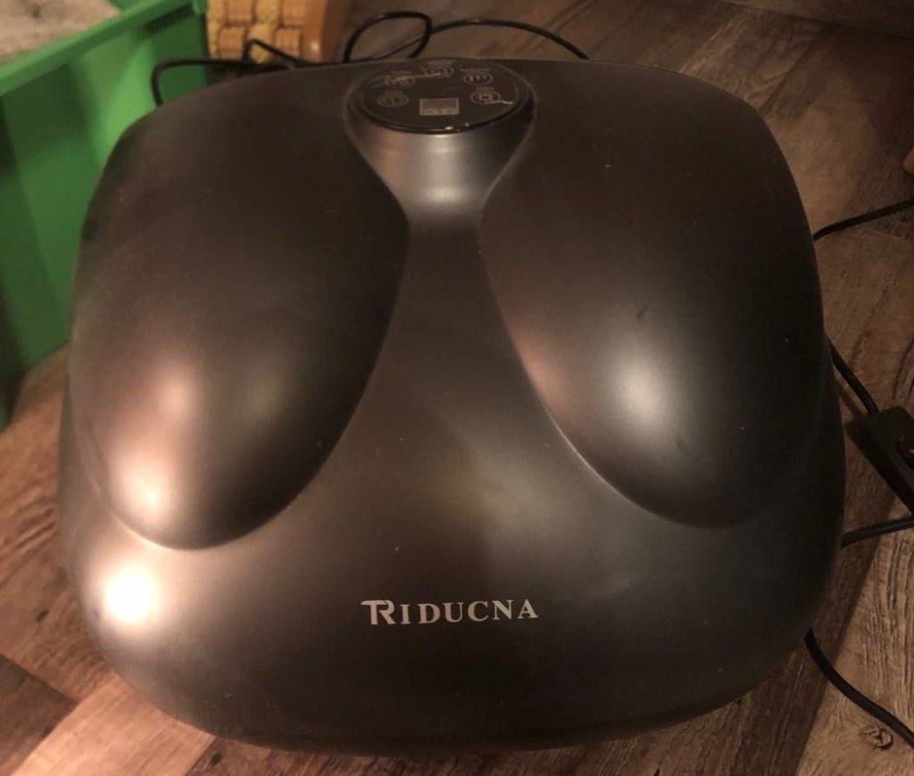Ein schwarzes Triducna Shiatsu Fußmassagegerät inklusive langem Kabel steht auf einem Holzboden.