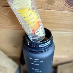 Ein gefüllter Fruchteinsatz wird in die Öffnung der 720°Dgree uberBottle eingesetzt. Die Flasche steht auf einem Holztisch.