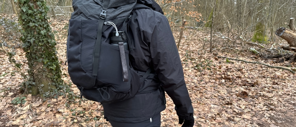 Die 720°Dgree Trinkflasche uberBottle steckt in der Seitentasche eines großen Wanderrucksacks. Ein Wanderer läuft durch einen herbstlichen Wald.