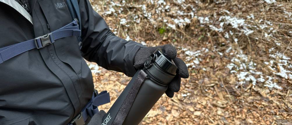 Eine Person hält die verschlossene 720°Dgree Trinkflasche uberBottle mit Handschuhen im Wald. Die schwarze Flasche ist vollständig geschlossen.