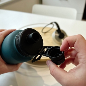 Eine Hand öffnet den kleinen Deckel der Trinkflasche.