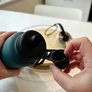 Eine Hand öffnet den kleinen Deckel der Trinkflasche.