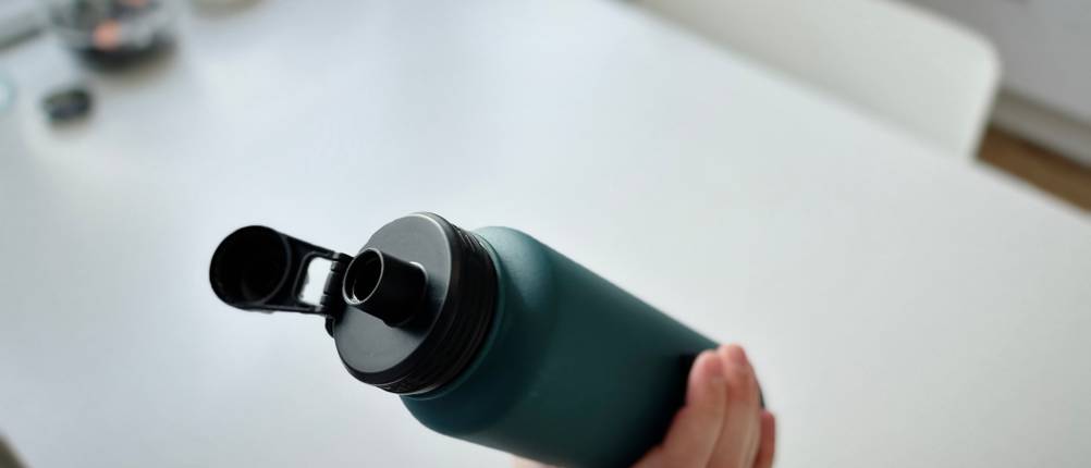 Eine Hand hält die Trinkflasche über einen weißen Untergrund.