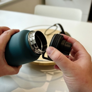 Zwei Hände halten die offnen Trinkflasche und den dazugehörigen Deckel.