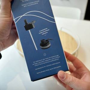 Zwei Hände halten die Verpackung der Trinkflasche Bemaxx.