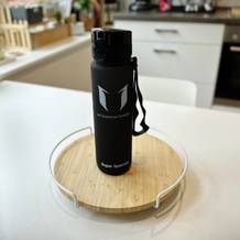 Eine Trinkflasche steht auf einer runden Scheide auf enem weißen Tisch.