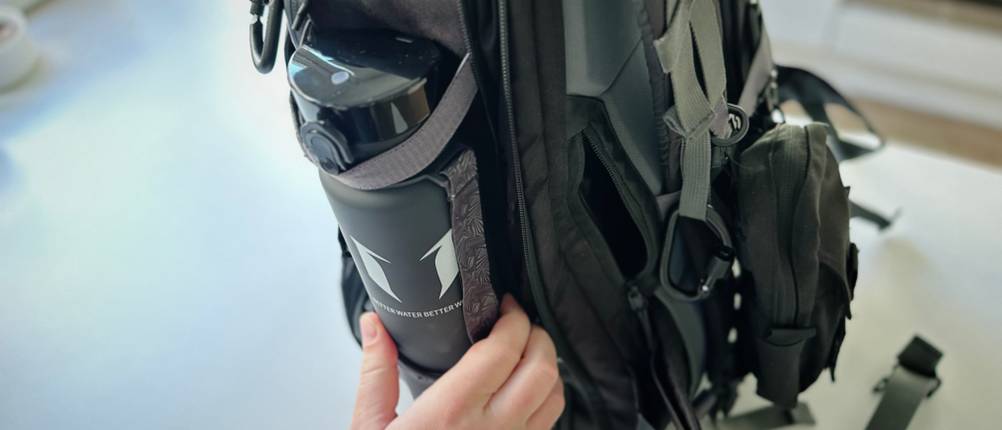 Die Trinkflasche wird in das Fach am Rucksack gesteckt.