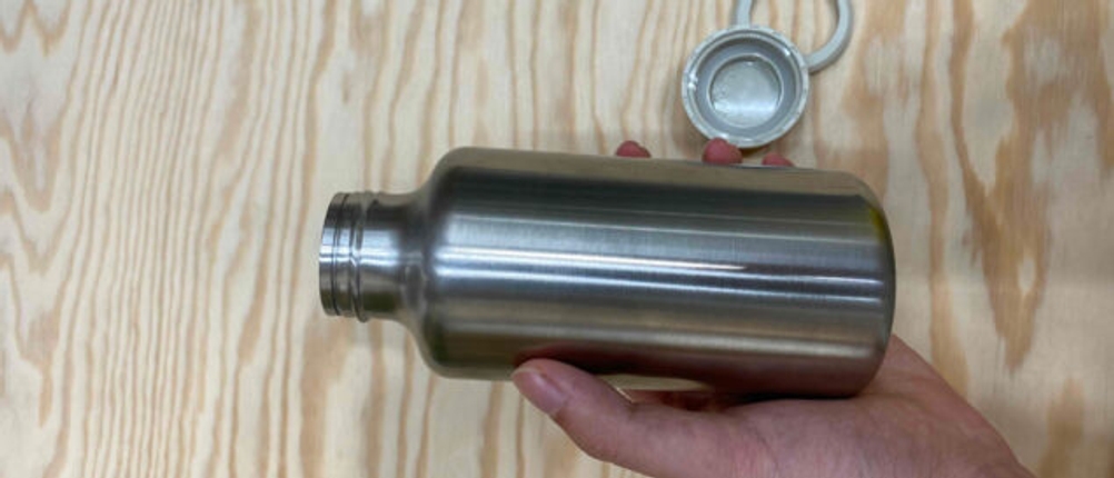 Eine Hand hält eine getestete Trinkflasche über eine Holzfläche.