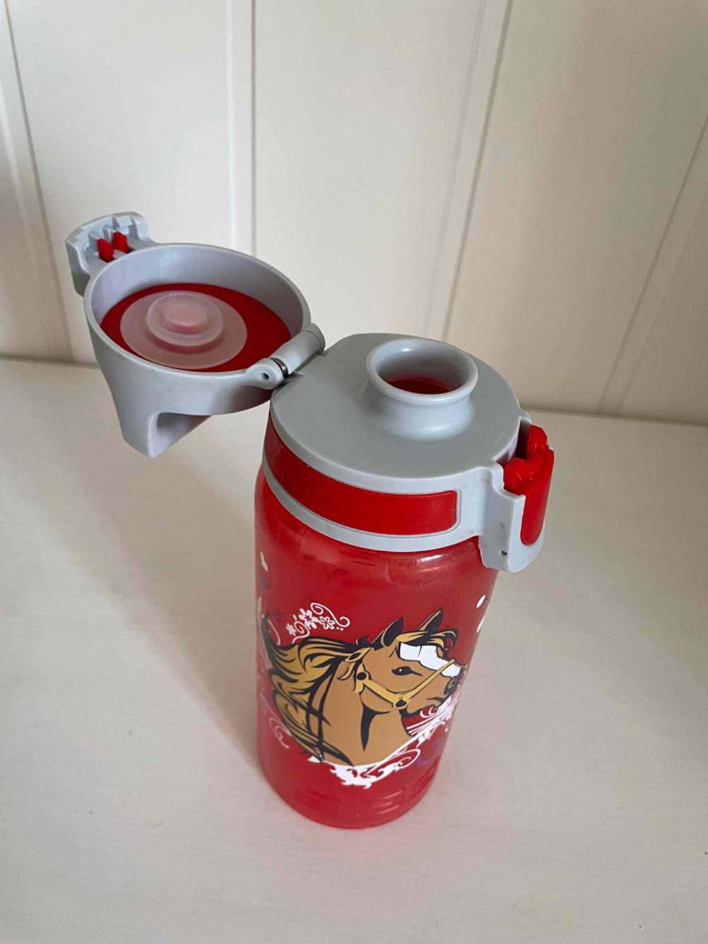 Eine getestete Trinkflasche für Kinder von schräg oben mit geöffnetetem Deckel auf einer hellen Fläche.
