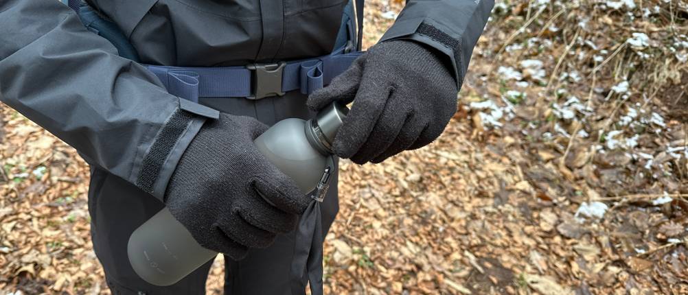 Eine Person im Wald öffnet die Mameido Tritan Trinkflasche mit einem Schraubverschluss.