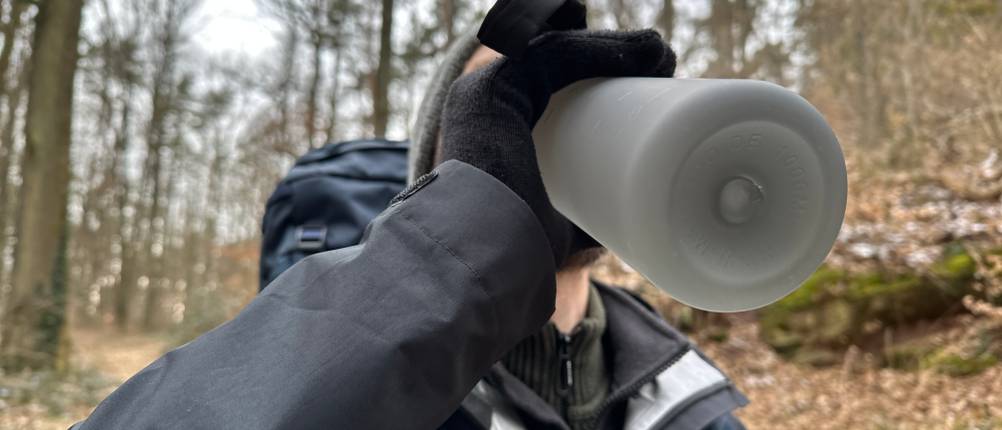 Eine Person trinkt aus der Mameido-Tritan-Trinkflasche beim Wandern im Wald.