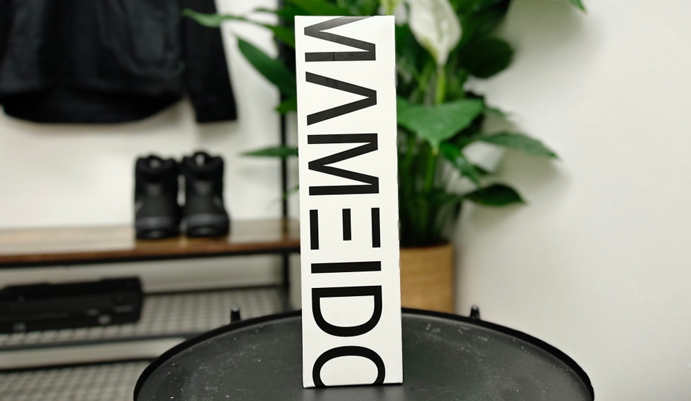 Die Mameido Tritan Trinkflasche steht mit ihrer weißen Verpackung auf einem Tisch. Der Markenname ist groß und vertikal aufgedruckt.