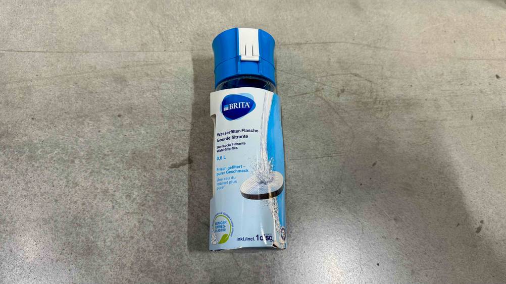 Auf einem Betonboden liegt eine getestete Trinkflasche mit Filter.