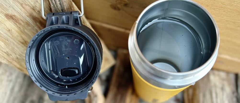 Geöffnete Stanley-Quick-Flip-Flasche neben dem abgeschraubten Deckel. Der Deckel liegt auf Holz, die Flasche ist mit Wasser gefüllt.