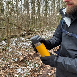 Eine Person hält die Stanley-Quick-Flip-Flasche mit beiden Händen. Der Deckel ist geschlossen, die Szene spielt im Wald.