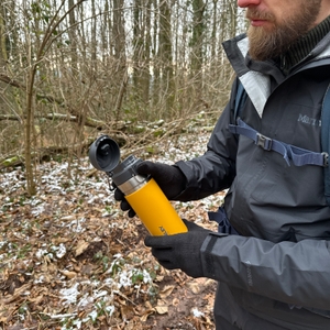 Die Stanley-Quick-Flip-Flasche wird geöffnet gehalten. Die Hand der Person zeigt auf den offenen Trinkverschluss.