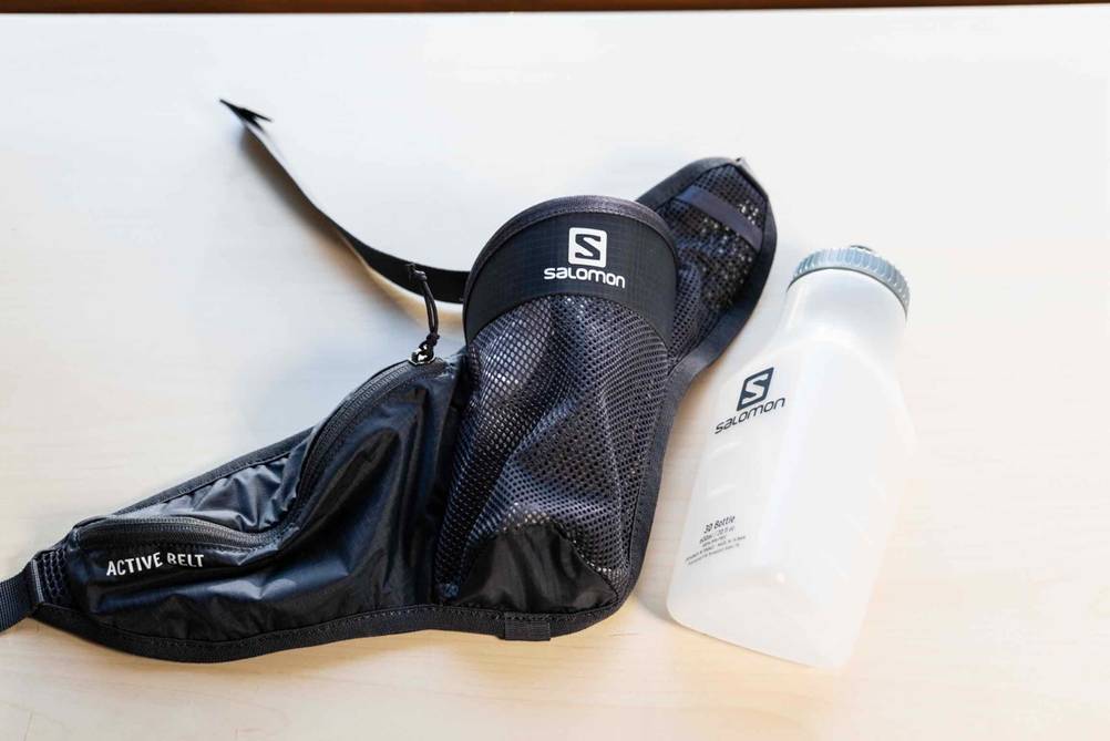 Neben einem getesteten Trinkgürtel liegt eine Trinkflasche auf einer hellen Oberfläche.