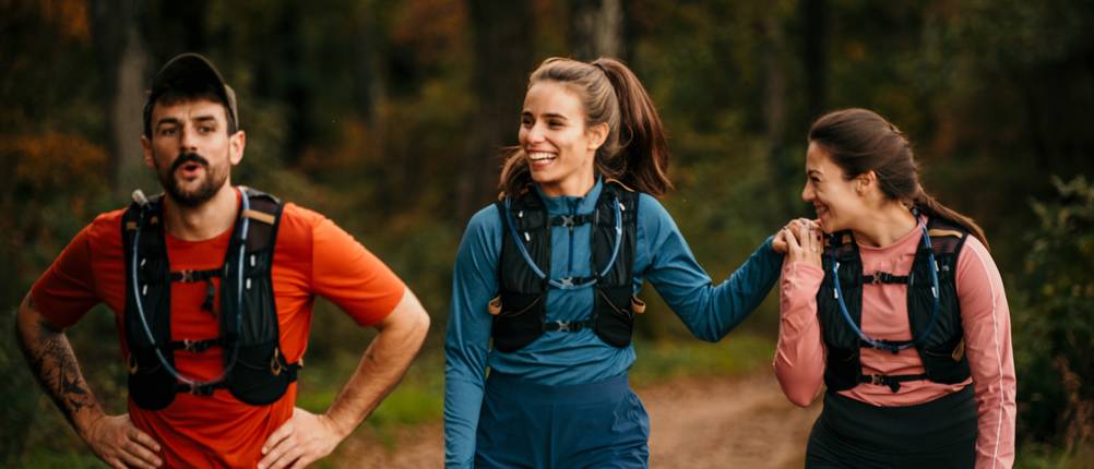 Mehrere Trinkwesten werden getestet von einem Mann und zwei Frauen beim Laufen im Wald.