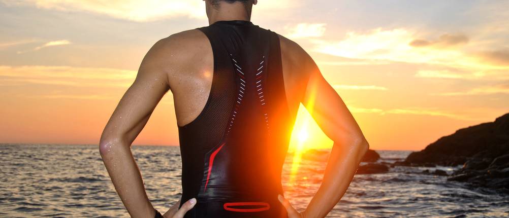 Trisuit-Herren-Test: Ein Mann steht bei einem Sonnenuntergang am Meer in einem Trisuit.