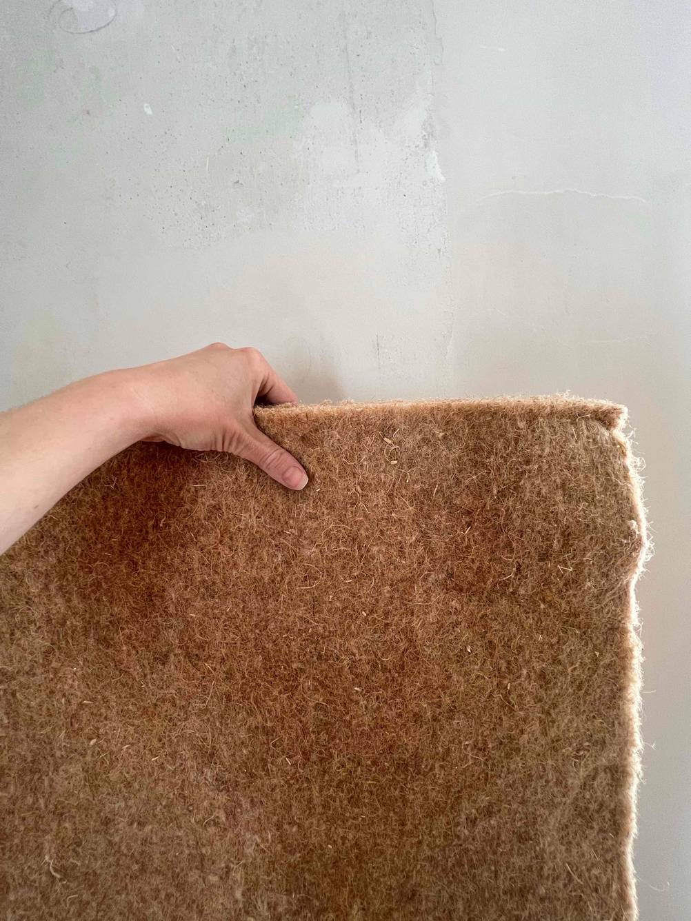 Trittschalldämmung getestet: Eine Hand hält eine Dämmung vor eine helle Wand.