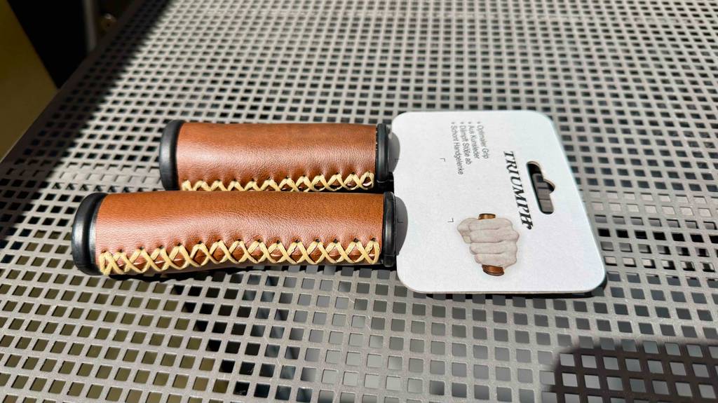 Zwei braune getestete Leder-Fahrradgriffe liegen auf einem Regalboden.