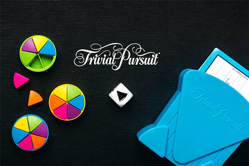 Trivial Pursuit im Test: Der blaue Fragekarten-Halter sowie die Spielsteine und ein Würfel auf schwarzem Untergrund.